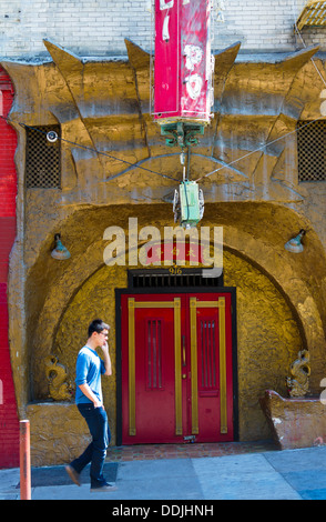 Young man on cellphone walking past ornate traditional Chinese entrance in Chinatown in San Francisco showing culture contrast Stock Photo