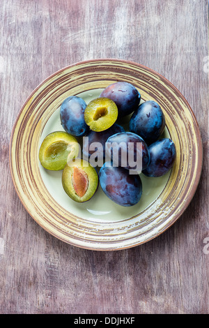 Fresh plums on plate over wooden background, overhead Stock Photo