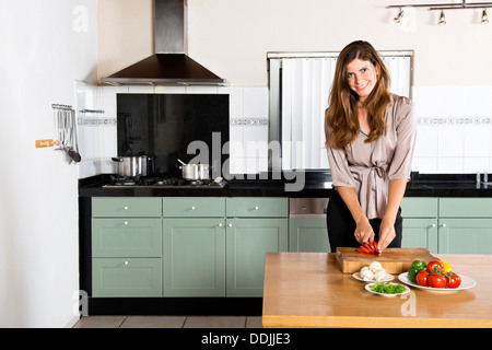 Portrait of beautiful young businesswoman chopping vegetables at kitchen counter Stock Photo