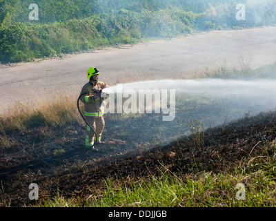 Fireman dousing down a grass fire, Kent, UK, summer Stock Photo