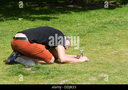 An amateur photographer crouches down to set up a compact camera on a small 'gorilla-pod' tripod. Stock Photo