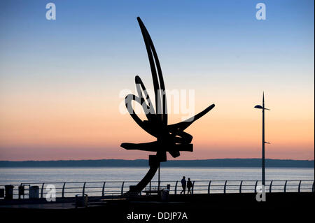 Port Talbot - South Wales - UK - 3rd September 2013 : People walking past the 'Kite Trail' sculpture as the sun sets along the seafront at Aberavon Beach near Port Talbot this evening. The Kite Trail sculpture at Aberavon seafront is Wales' largest sculpture standing at 12 metres high and weighing 11 tonnes. It was designed by Carmarthenshire-based artist and sculptor Andrew Rowe and was installed in December 2007. © Phil Rees/Alamy Live News Stock Photo