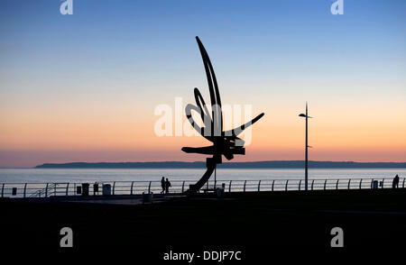 Port Talbot - South Wales - UK - 3rd September 2013 : People walking past the 'Kite Trail' sculpture as the sun sets along the seafront at Aberavon Beach near Port Talbot this evening. The Kite Trail sculpture at Aberavon seafront is Wales' largest sculpture standing at 12 metres high and weighing 11 tonnes. It was designed by Carmarthenshire-based artist and sculptor Andrew Rowe and was installed in December 2007. © Phil Rees/Alamy Live News Stock Photo