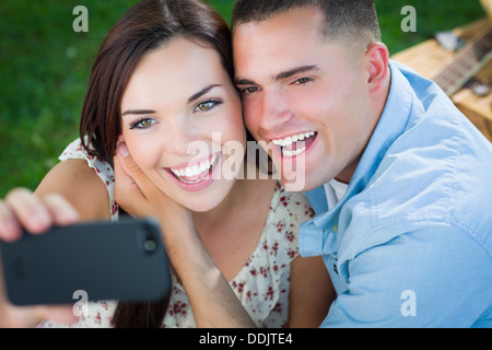 Happy Mixed Race Couple Taking Self Portrait with A Smart Phone in the Park. Stock Photo