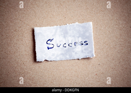 Success message,written on piece of paper, on cardboard background. Space for your text. Stock Photo