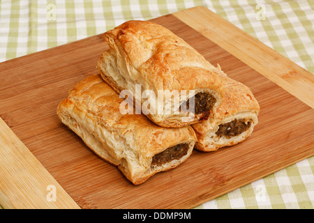 Three traditional sausage rolls on a rustic cafe table setting, a popular pastry snack available from british bakers Stock Photo