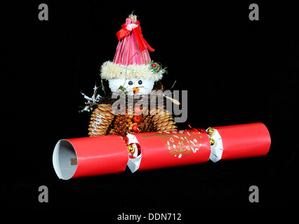 Snowman made from pinecones with a red Christmas cracker set against a black background. Stock Photo