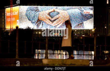 Berlin, Germany. 04th Sep, 2013. A woman stands in front of a giant election poster for the election campaign of German chancellor Angela Mekel showing her typical hand position in Berlin, Germany, 04 September 2013. Germany holds general elections on 22 September. Photo: Kay Nietfeld/dpa/Alamy Live News Stock Photo