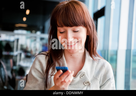 Woman texting on mobile phone and smiling, sitting in a cafe Stock Photo