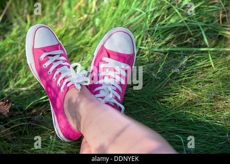Woman wearing pink trainers with legs crossed outside - point of view Stock Photo