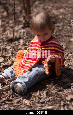 little girl wearing a striped sweater plays in the leaves Stock Photo