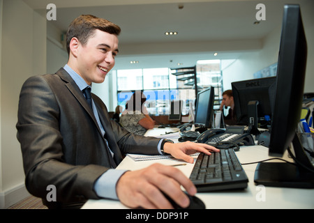 A happy attractive well dressed young suited male office worker enjoying work, or is he social networking or gaming? Stock Photo