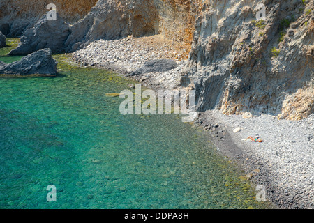 A woman sunbathing on a rocky beach below Punta Milazzese on Panarea in the Aeolian Islands, Messina, Sicily, Italy Stock Photo