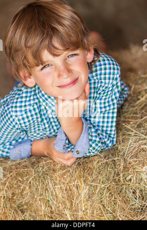 Young happy smiling boy wearing a plaid shirt and laying on bales of hay or straw Stock Photo