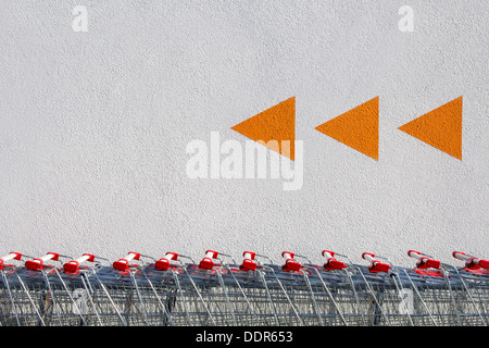 A row of shopping Carts and orange arrows painted on a white wall Stock Photo