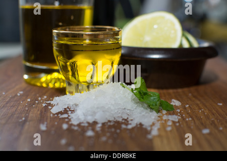 Heap of sea salt, coriander, olive oil in a small shot glass and slices of lime in a small dark brown stoneware bowl on oak. Stock Photo