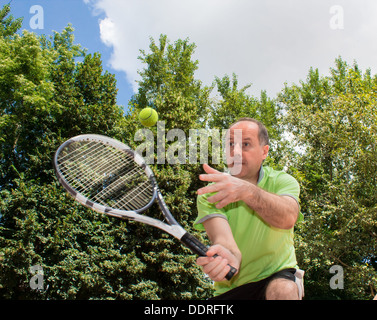 Tennis player in the movement against the beautiful green trees and cloudy sky on a sunny day Stock Photo