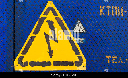 High voltage yellow sign mounted on blue metal rabitz grid with blue metal wall on background Stock Photo