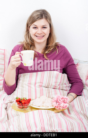 Happy smiling young woman with cup of coffee enjoying romantic breakfast in bed. Stock Photo