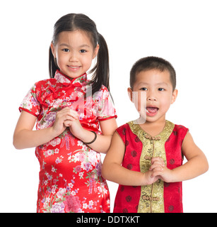 Little oriental girl and boy wishing you a happy Chinese New Year, with traditional Cheongsam standing isolated on white background. Stock Photo