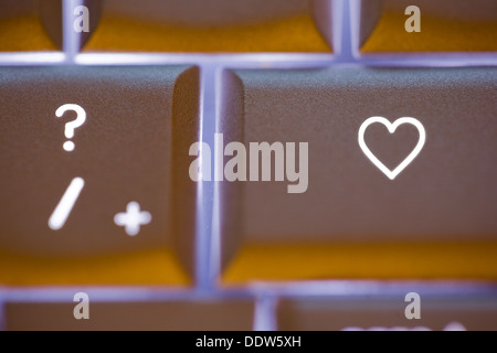 close-up of an illuminated computer keyboard with a heart shaped symbol on the key next to the question mark. Stock Photo
