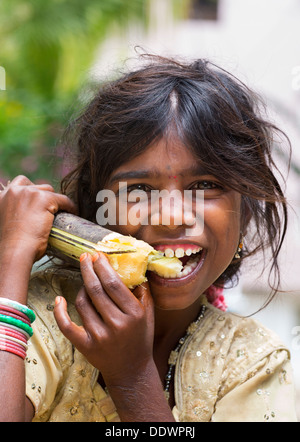 Young poor lower caste Indian street girl biting into sugar cane. Andhra Pradesh, India Stock Photo