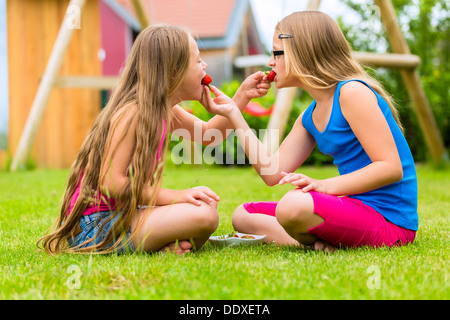 Happy Girls or sisters playing at home in garden and eating strawberries Stock Photo