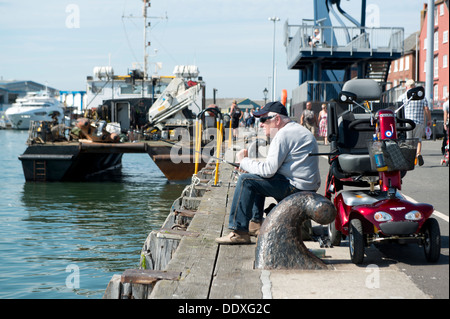 A pensioner sits fishing by the quay in Poole in the county of Dorset in southern England. Stock Photo