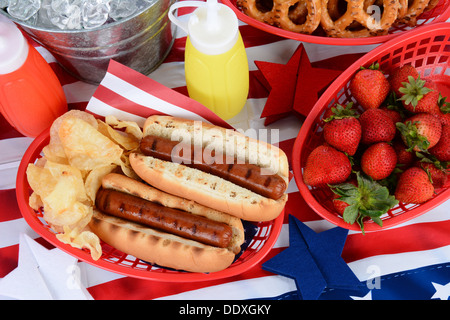 Looking down on a picnic table decorated for the 4th of July. Hot Dogs, chips, strawberries, mustard, ketchup. Stock Photo