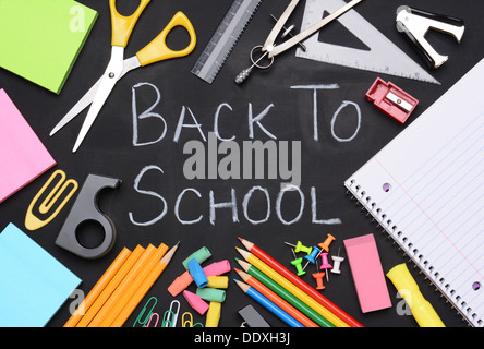 Back to school written on a chalkboard. The words are surrounded by school supplies including, paper, scissors, pencils, Stock Photo