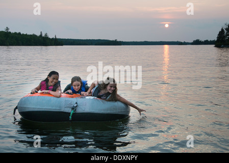 Three girls enjoying on inflatable raft in the lake, Lake Of The Woods, Keewatin, Ontario, Canada Stock Photo