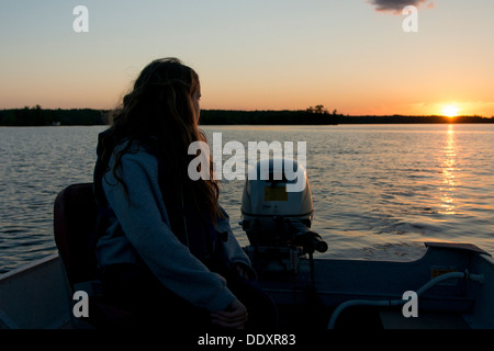 Girl sitting on a motorboat in the lake at sunset, Lake of The Woods, Keewatin, Ontario, Canada Stock Photo