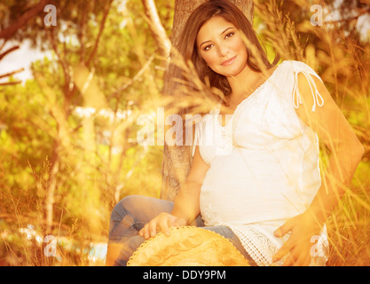 Pregnant woman in autumn park, beautiful expectant female relaxing outdoors in sunny autumnal day, happy and healthy pregnancy Stock Photo