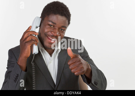 Young black man in a suit making a phone call in an office, smiling with thumbs up gesture Stock Photo