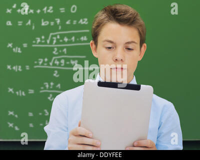 Portrait, schoolboy, teenager with an iPad in front of a school blackboard with a mathematical equation Stock Photo