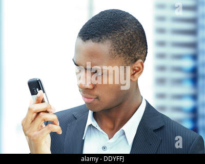 Young businessman, African-American, American, looking at his mobile phone, checking texts, focused Stock Photo