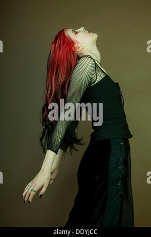 Woman with red streaks in her hair, Goth subculture, standing with her arms bent back Stock Photo