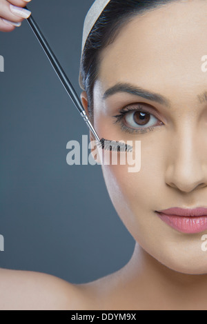 Cropped image of beautiful young woman using eyebrow tinting applicator over colored background Stock Photo