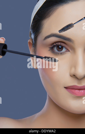 Cropped image of pretty young woman with mascara and eyebrow tinting applicator over colored background Stock Photo
