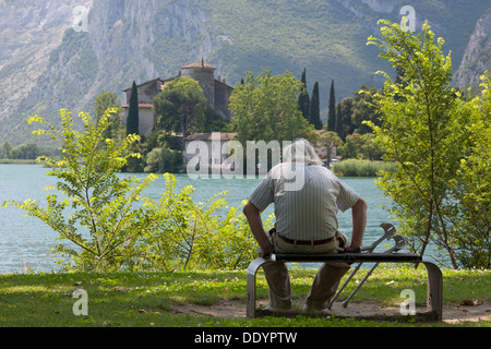 Old man pause on a park bench and enjoys the view of the castle Toblino Stock Photo