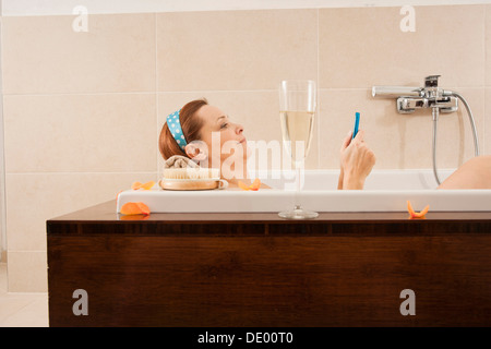 Woman using a mobile phone in the bathtub Stock Photo