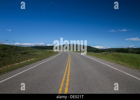 Scenic, dramatic, low level landscape of highway curving to left, with deep blue sky. Double yellow line. Stock Photo