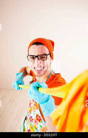 Young man wearing an apron and cleaning gloves holding a cleaning mop Stock Photo