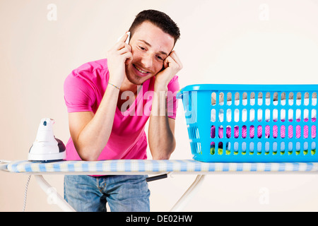 Young man talking on the telephone while leaning on an ironing board Stock Photo