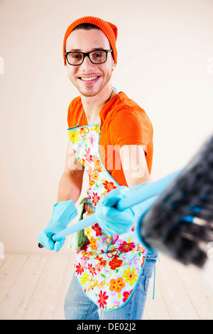 Young man wearing an apron and cleaning gloves holding a broom Stock Photo