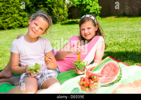 Two sisters eating lettuce and watermelon in the garden Stock Photo
