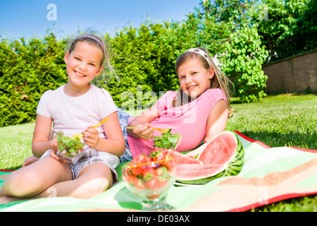 Two sisters eating lettuce and watermelon in the garden Stock Photo