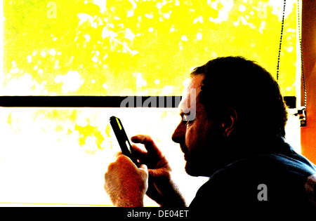 close up of man texting on an iphone silhouetted against a window in Cafe Stock Photo