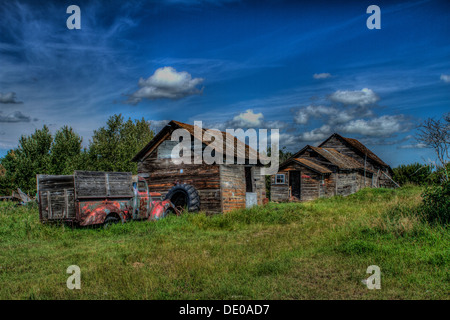 An old, abandoned truck, sitting in a farmyard, by old buildings, againt a blue sky. Dramatic blue sky and rich colors Stock Photo