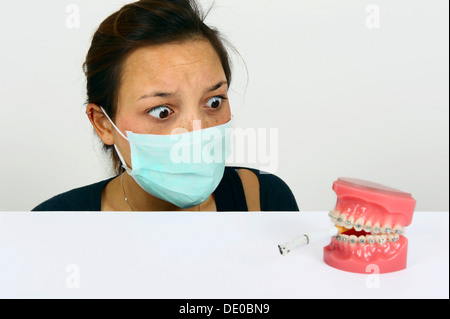 Symbolic image for adolescent smokers, young woman looking in horror at dentures with fixed braces and a smoking cigarette